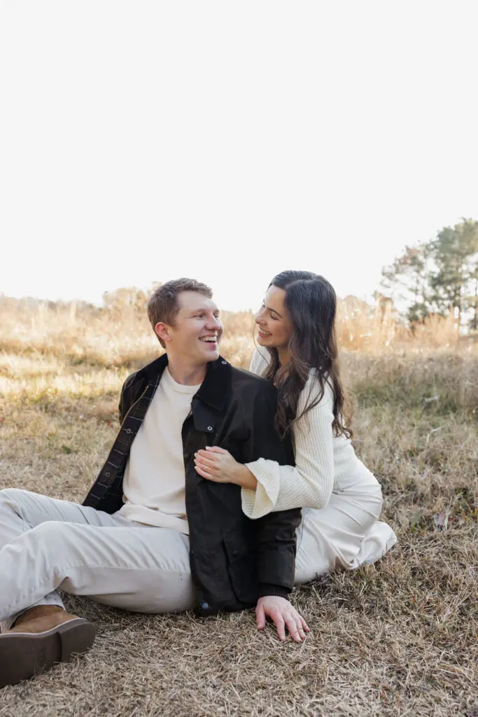Wide shot of an engaged couple in a peaceful field at Bells Mill Park, surrounded by greenery and wearing neutral tones.