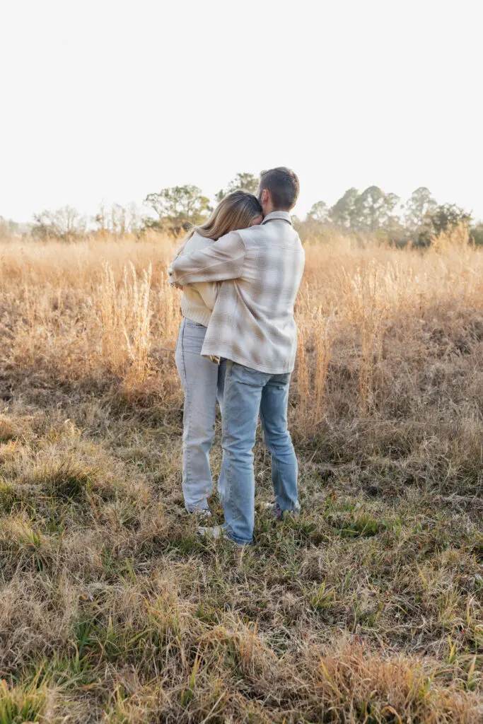 Couple showing engagement ring while standing in a winter field at Bells Mills in Chesapeake near Virginia Beach.
