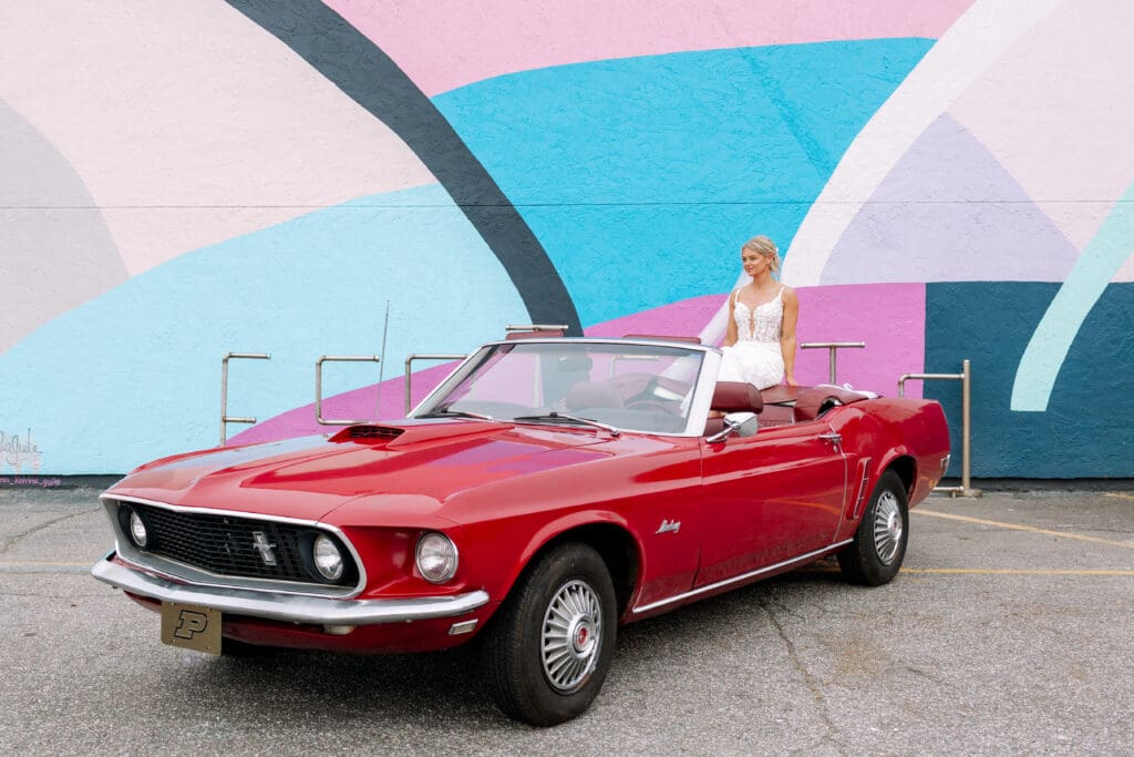 A bride sitting on a red ford mustang convertible