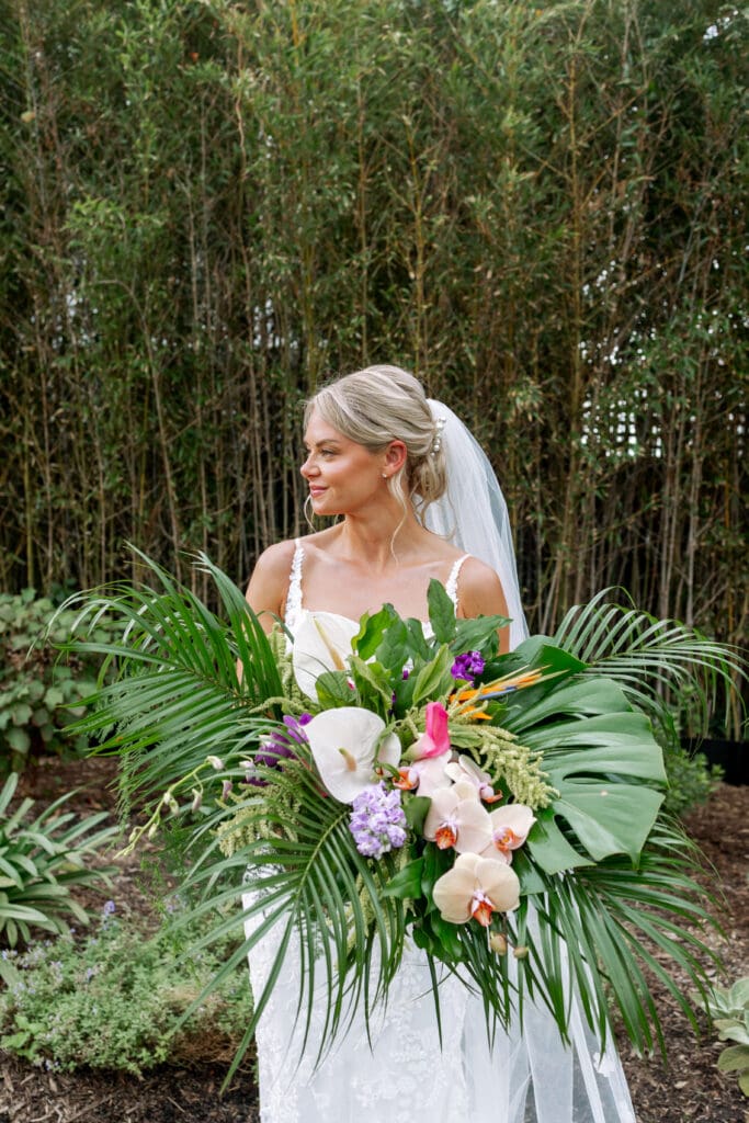 A bride holding a very large tropical bouquet looking to her left