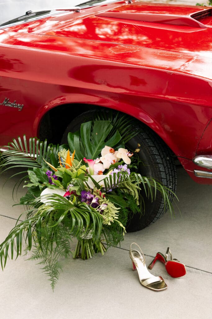 A red ford mustang parked by a large tropical bouquet and Louboutin heels 