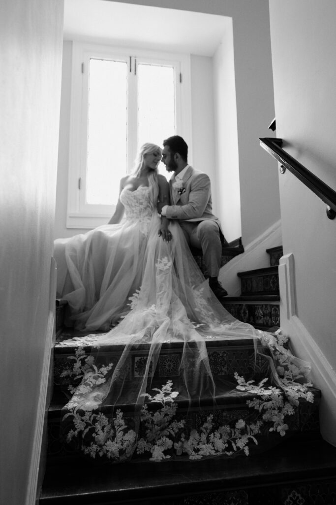 Black and white portrait of the bride and groom with a long cathedral lace veil handing down the Alderman House steps 