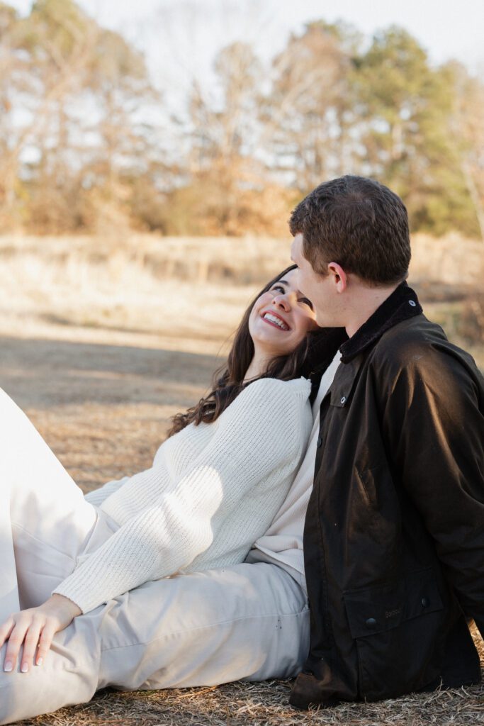 Engaged couple laughing together in an open meadow at Bells Mill Park, wearing neutral outfits under natural light.