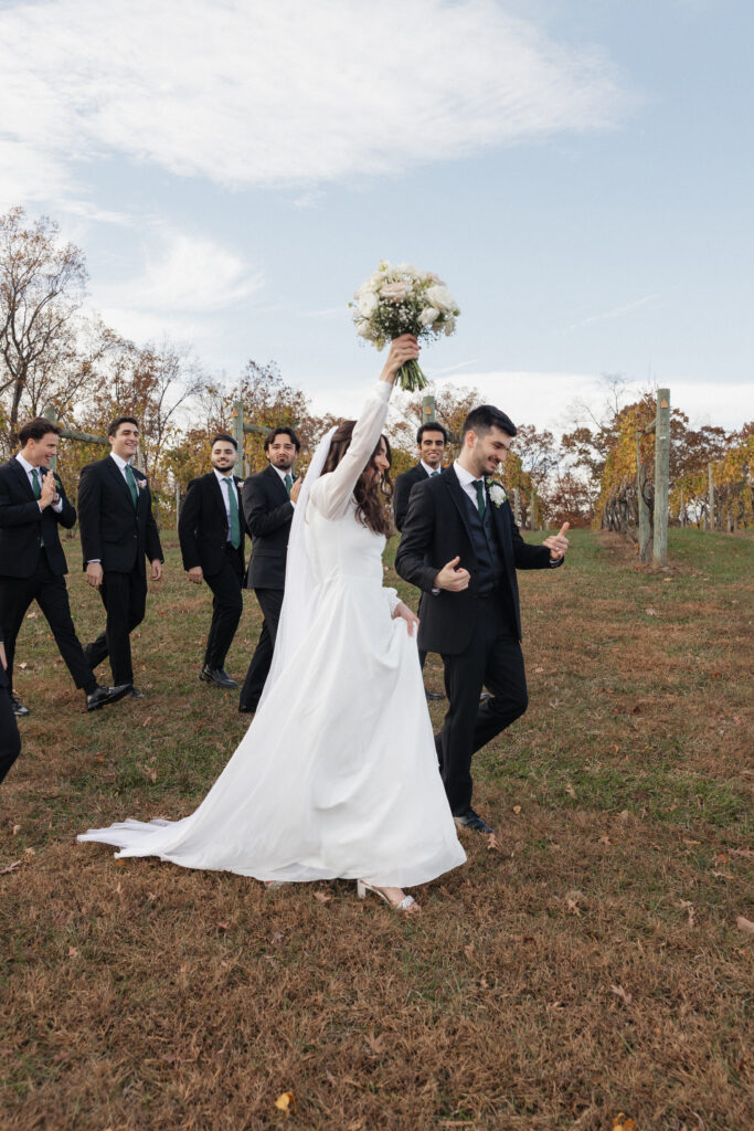 Large wedding party group photo posed on the scenic grounds of Lovingston Winery mountain vineyard near Charlottesville Virginia with rolling hills and lush grapevines in the background