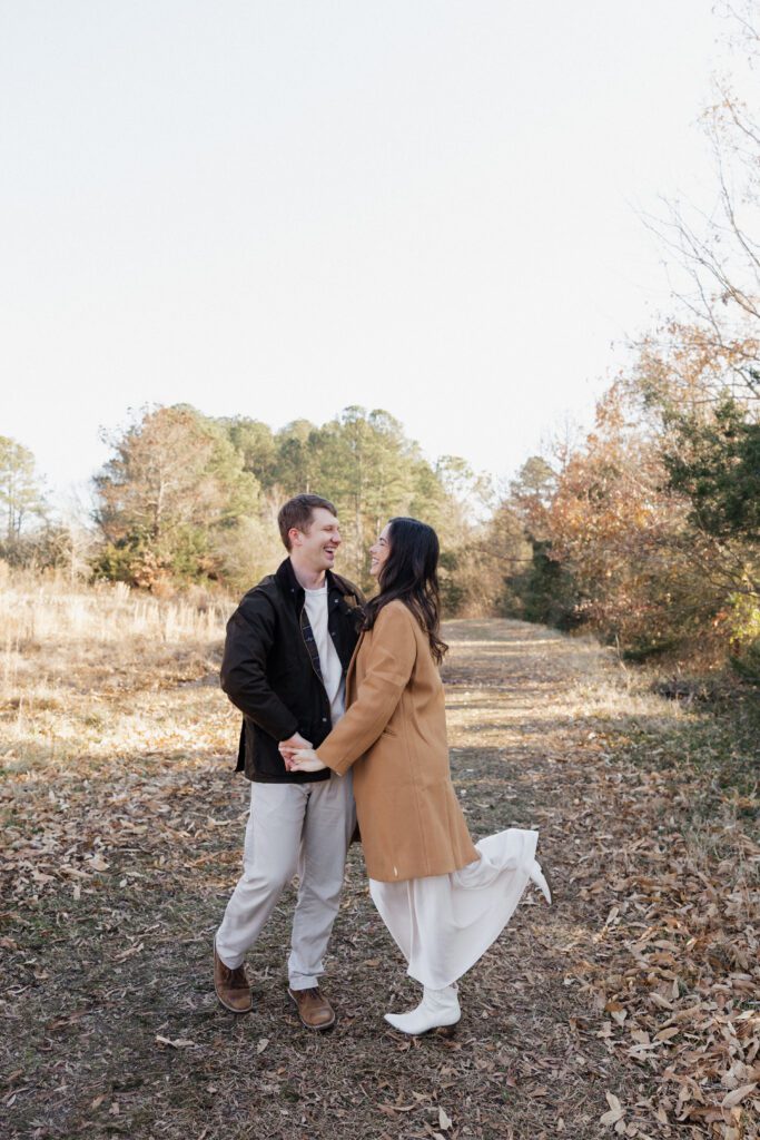 Engagement photo of a couple walking through a sunlit field at Bells Mill Park in Chesapeake, dressed in beige and earth tones.”