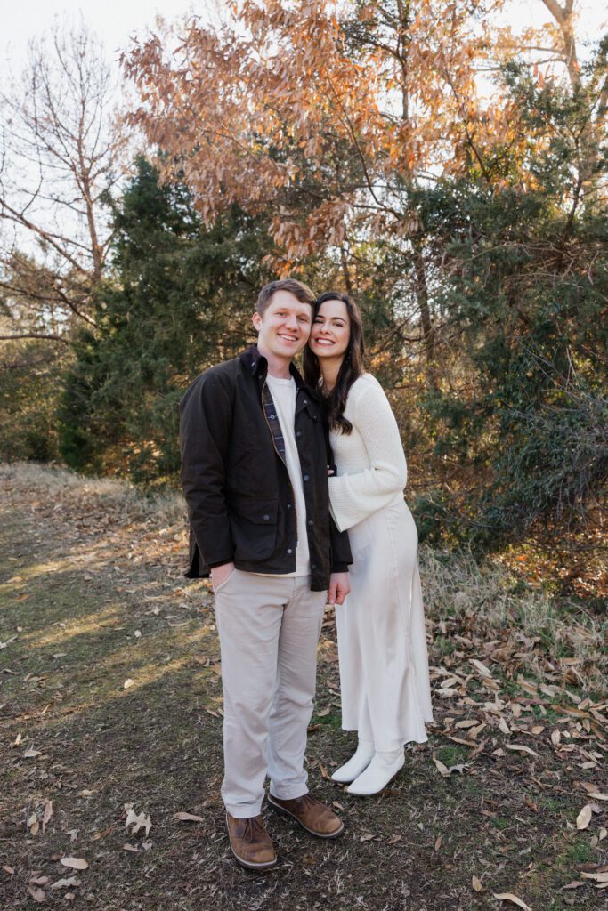 Engaged couple in neutral-toned outfits standing close together in an open field at Bells Mill Park in Chesapeake, Virginia.”