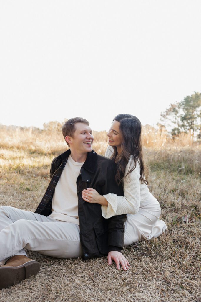 Wide shot of an engaged couple in a peaceful field at Bells Mill Park, surrounded by greenery and wearing neutral tones.