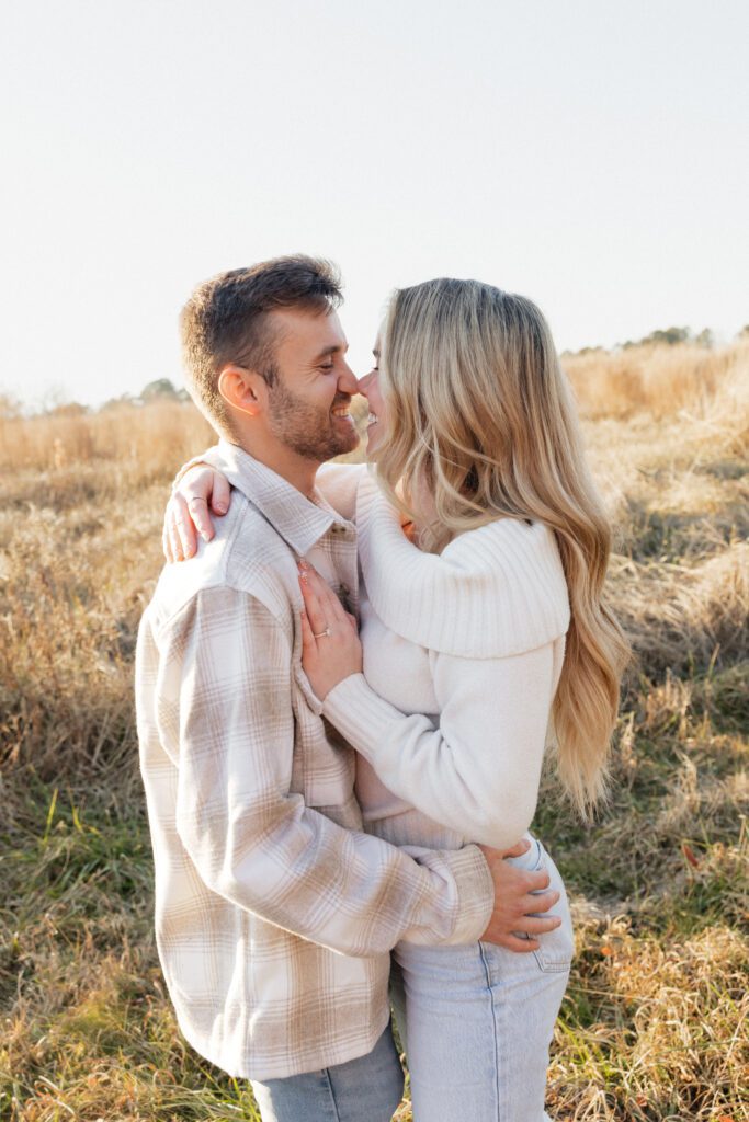 Couple embracing during a winter engagement session at Bells Mills in Chesapeake, Virginia, surrounded by open fields.